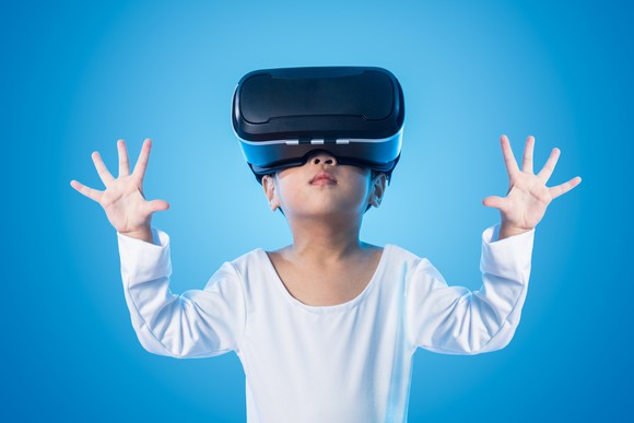 A little boy with a VR headset on in front of a blue screen.