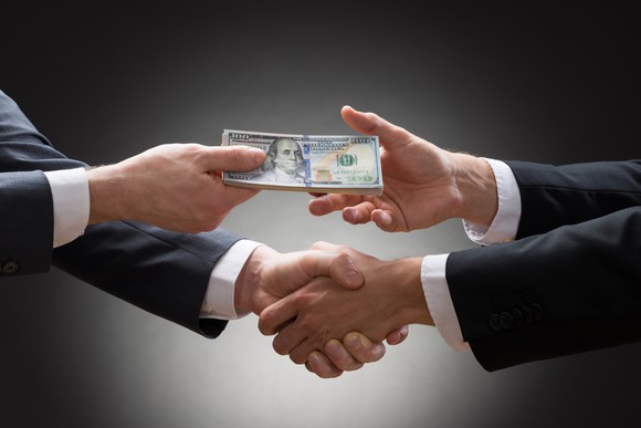 Two business people shake hands while exchanging money.