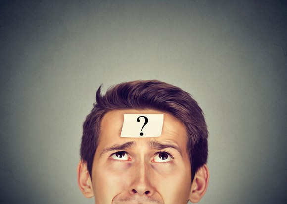 A man looks up at a sticky note with a question mark located on his forehead.