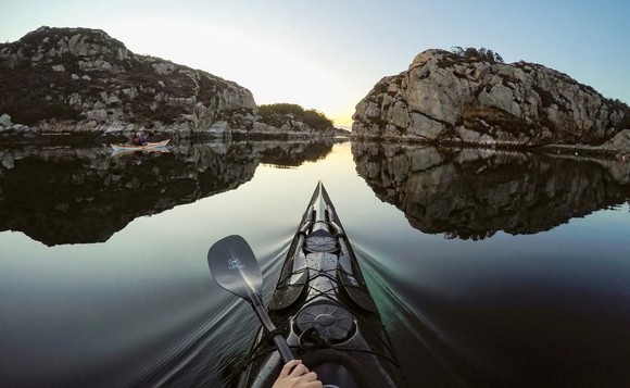 Picture from point of view of person in kayak looking at a lake smooth as glass just before sunrise and two rock islands ahead.