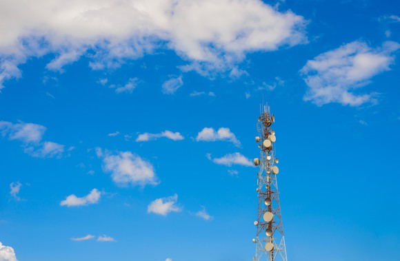 A cell phone tower, equipped with many antenna dishes, set against a partly cloudy sky.