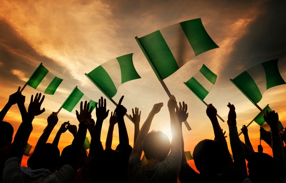Group of people waving the Nigerian flag as the sun sets in the distance.