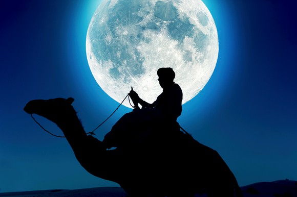 Tuareg man on camel at night with moon in background.
