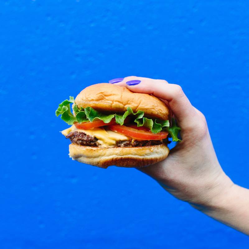 A hand holding a large cheeseburger.