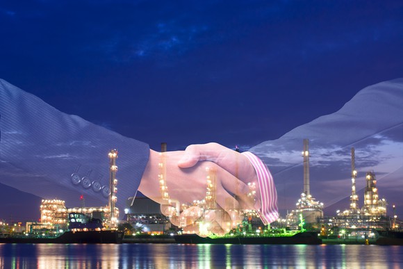 Shaking hands in front of a refinery.
