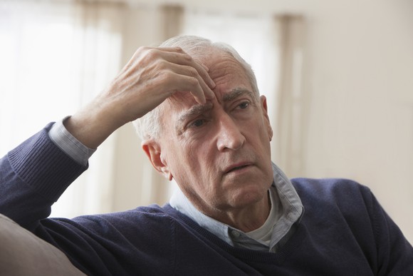 A worried senior citizen puts his hand to his forehead as he gives a concerned expression.