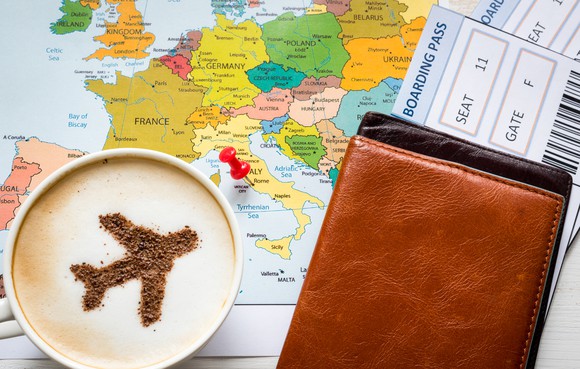A plane is seen in the foam on a cup of coffee sitting next travel documents.