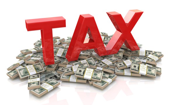 Big red letters spelling tax sit atop a pile of money.