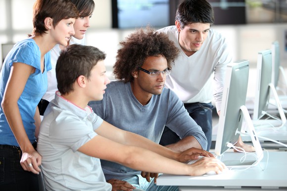 Young people cluster around a computer monitor