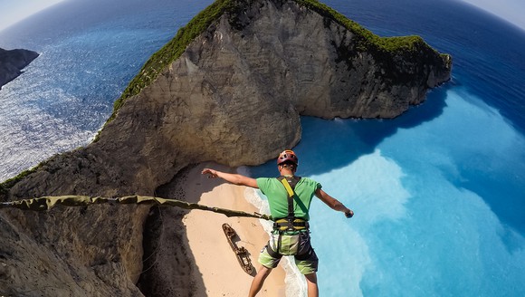 Guy in harness and helmet attached to a bungee chord high above a beautiful view of a clear blue ocean and a rock island.