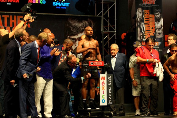 Floyd Mayweather standing on a scale for a weigh in, surrounded by people.