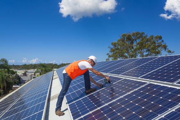 A technician on a roof securing solar panels to it.