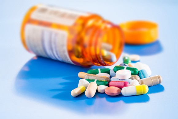 Pill bottle spilling an assortment of pills on a blue counter.