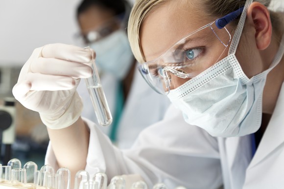 A biotech lab researcher holding and examining liquid in a test tube.