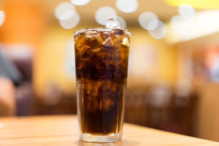 Glass of Coke with ice on wooden table, with background "bokeh" soft lighting effect.