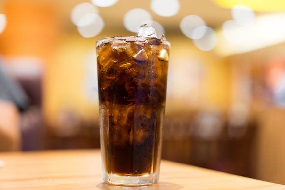 Glass of Coke with ice on wooden table, with background "bokeh" soft lighting effect.