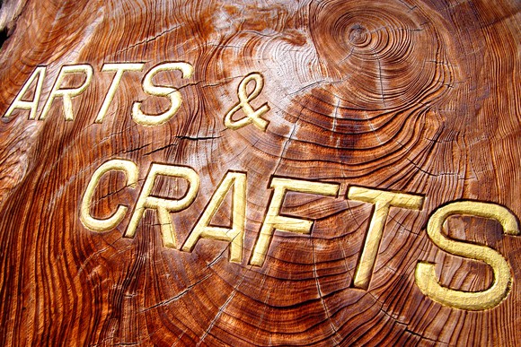 "Arts & Crafts" written in carved-out gold letters on a dark, textured block of wood.