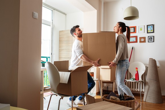 young man and woman carrying a large cardboard box through a house