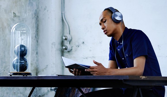 A man wearing Sony headphones sits reading at a table