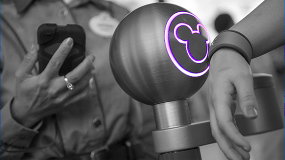 A guest wearing a MagicBand triggers an entrance turnstile at a Disney World park.