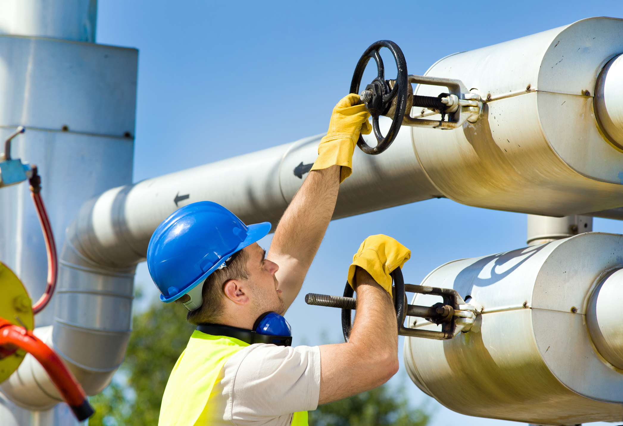 A man in a hard hat turning valves on a pipeline