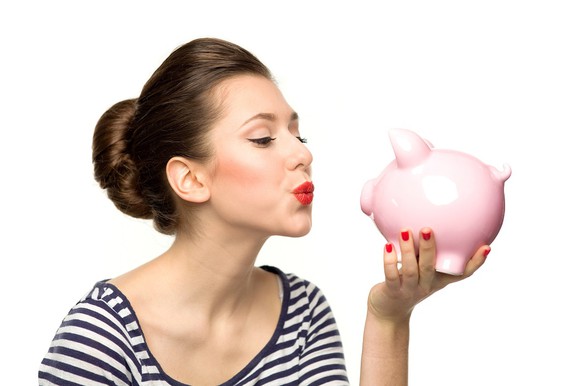 A woman puckers her lips at a piggy bank in her hand.