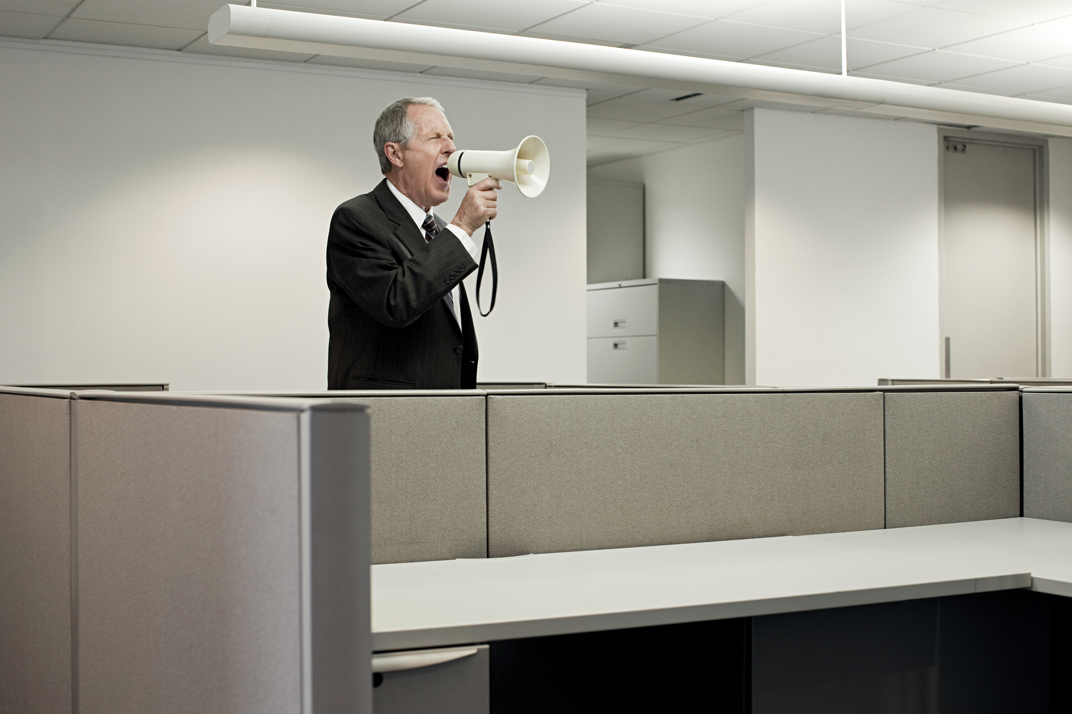 man in suit shouting through a foghorn in an empty office.