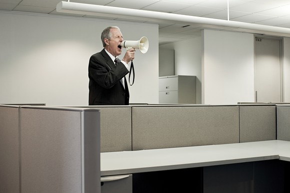 man in suit shouting through a foghorn in an empty office.