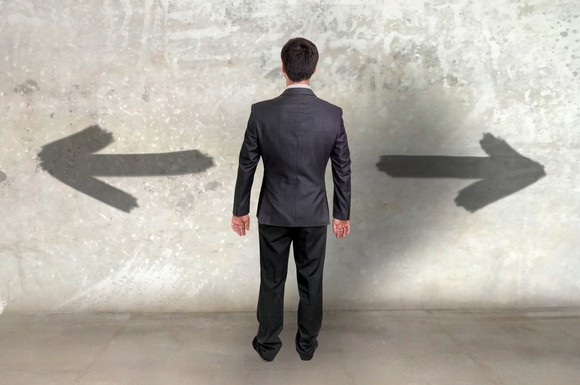 Man dressed in suit facing arrows on wall pointing left and right