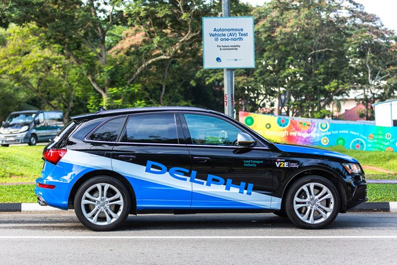 A blue and black Audi station wagon with Delphi logos and self-driving sensor hardware, on a suburban street.