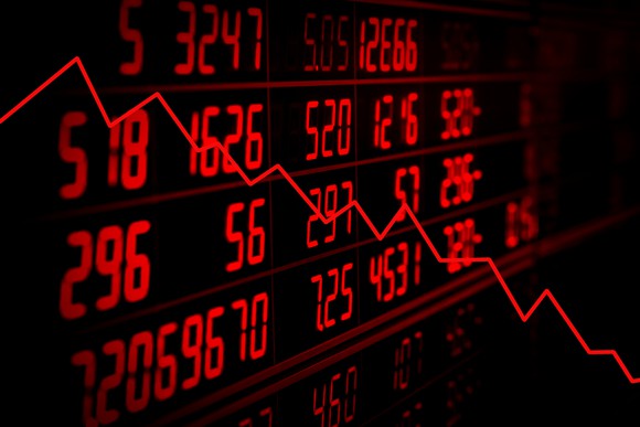 Downward trend arrow with stock ticker board in background.
