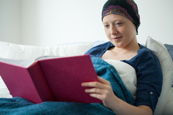 A female cancer patient in bed reading a book and smiling