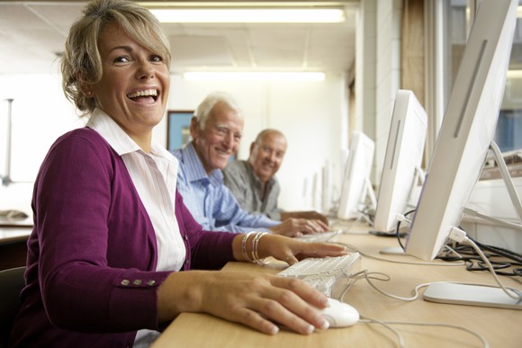 Seniors using computers at a long table.