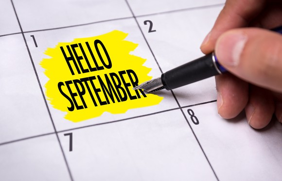 Hand holding pen next to words "Hello September" highlighted in yellow on calendar