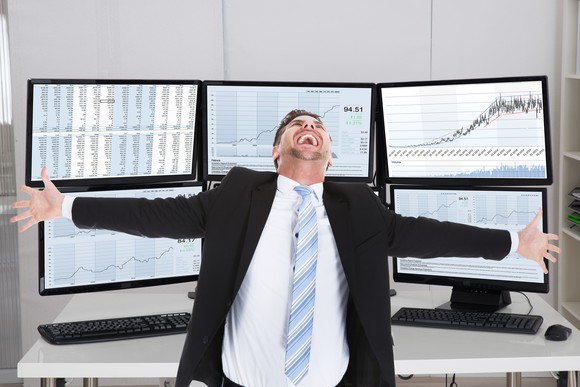 Super happy investor standing in front of monitors displaying upward rising charts.