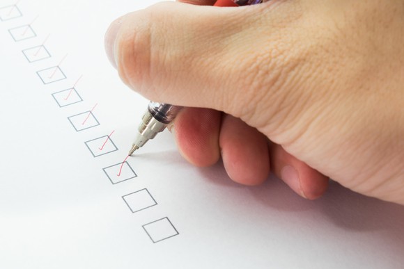 A hand holding a red pen checks off a column of boxes.