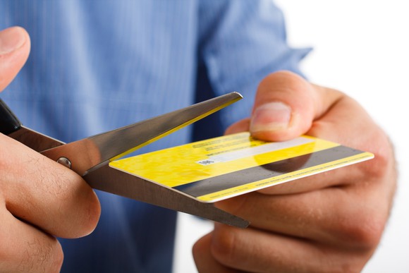 close up of two hands holding and cutting a credit card, with scissors