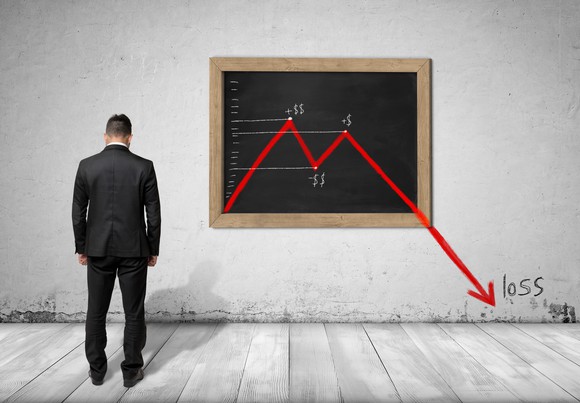 A businessman looking into the field of view with his head down, a red chart showing losses is drawn on a chalkboard.