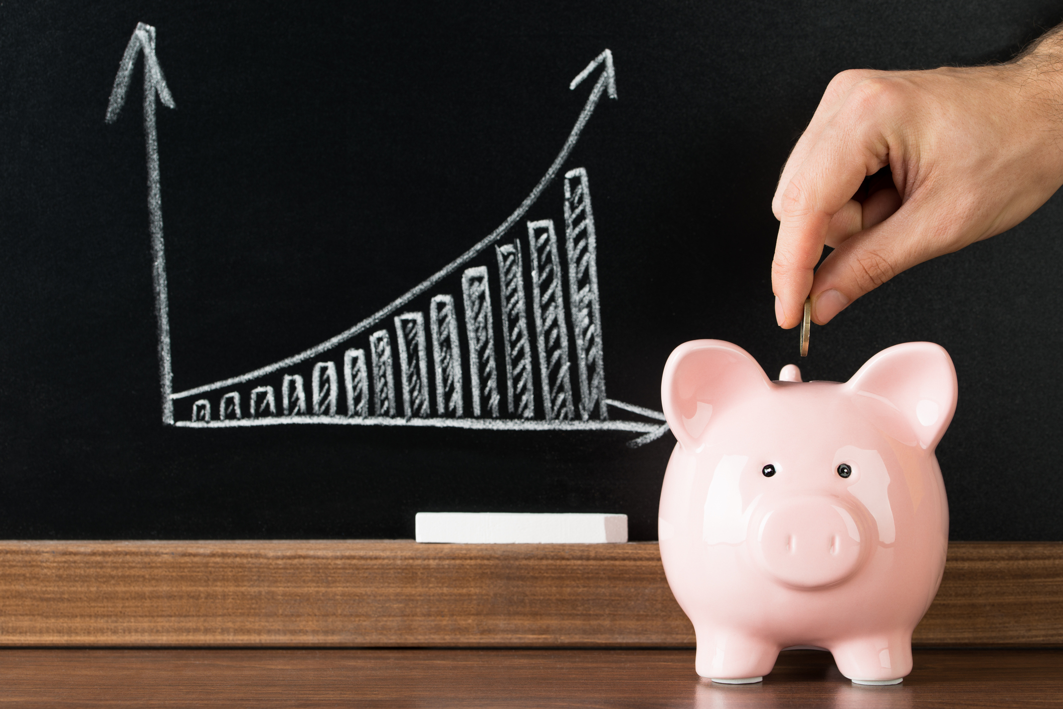 Man putting a coin in a piggy bank with a chart of growing value over time in the background.