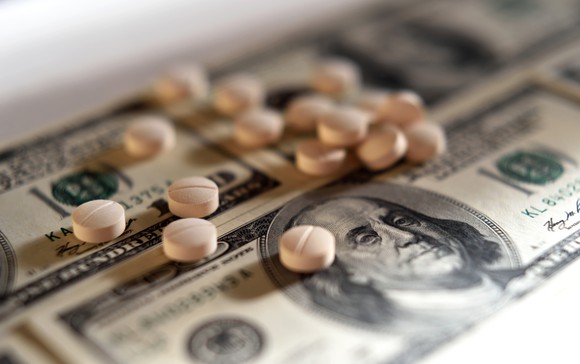 A small pile of pills on top of hundred dollar bills.