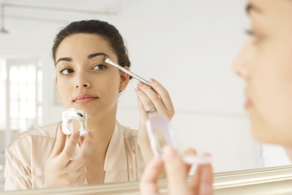 A woman applies makeup in a mirror.
