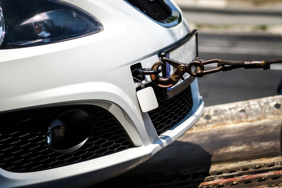 White sports car being towed with close-up of metal towing hitch.