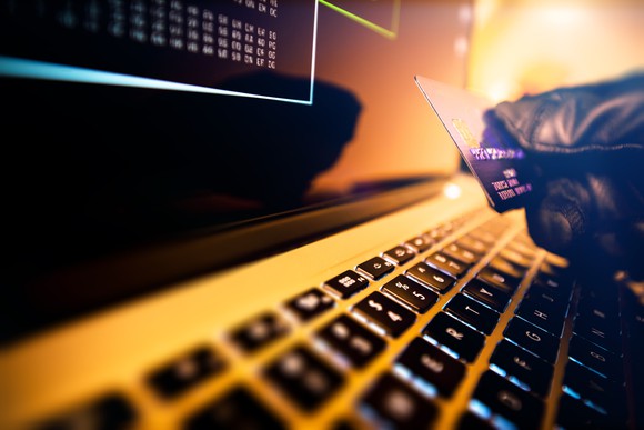 A glove hand holding credit card over a computer keyboard.