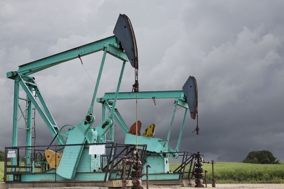 Two green oil wells sitting under a dark stormy grey sky in the summertime.