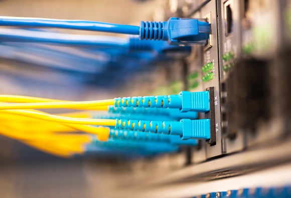 Several Ethernet and fiber optic networking cables, plugged into a large-scale networking switch.