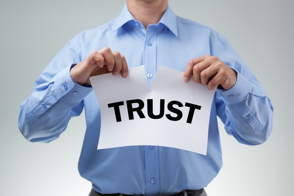 A man tearing up a sheet of paper with "Trust" printed on it.