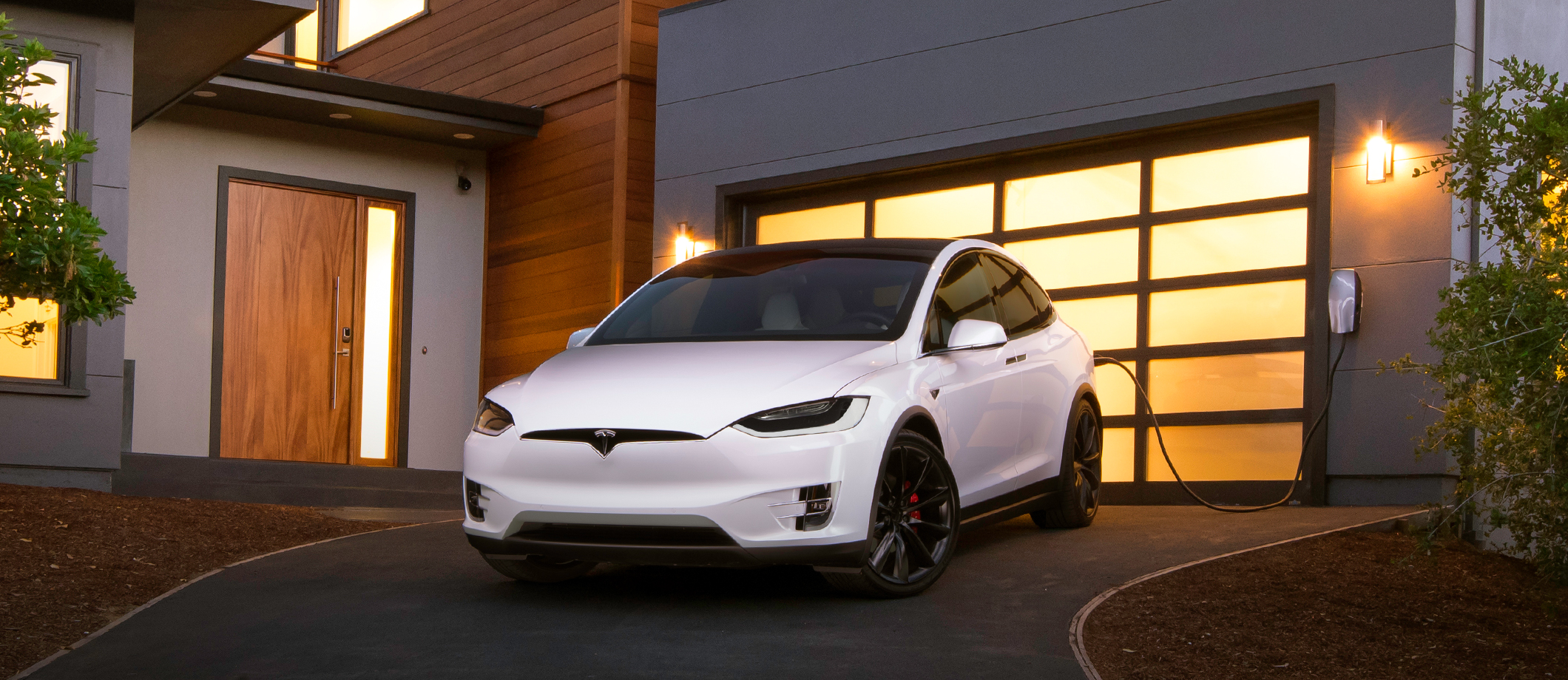 A white Tesla Model X charging at home in a driveway.