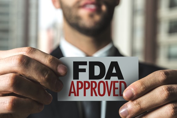 A man in a suit holding a card that reads "FDA Approved."