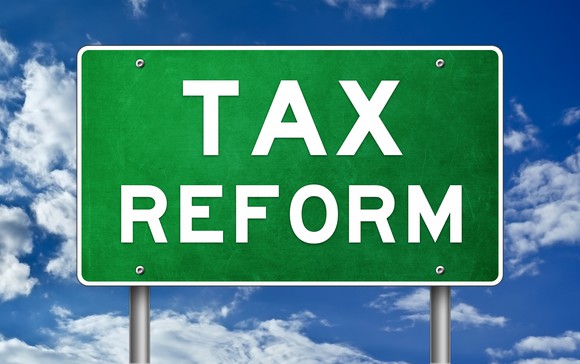 A green road sign with the words "tax reform" on it, sitting against a blue sky.