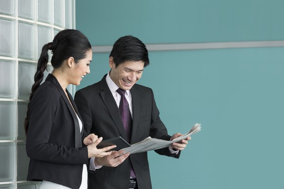 A businessman and businesswoman read the newspaper.